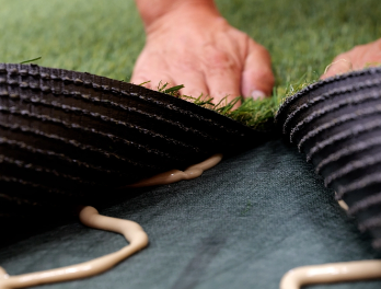 Hands folding artificial turf down onto the adhesive bead and seam tape