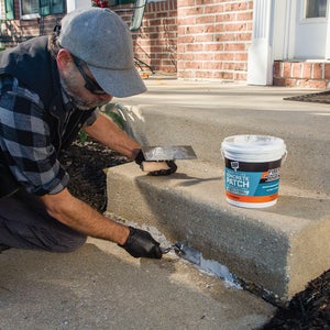 Installer patching the broken edge of a concrete step with the tub beside him