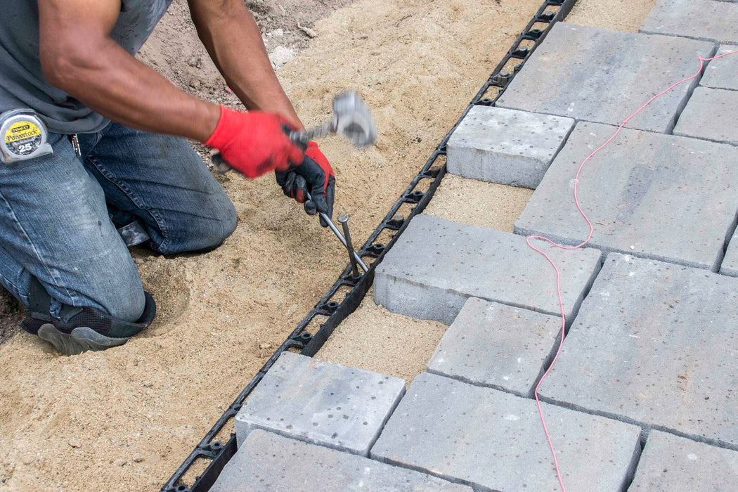 Driving a steel spike through SEK paver edge restraint into the compacted base