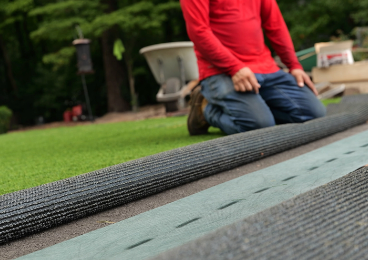 Installer rolling out seam tape along the joint between two pieces of artificial turf