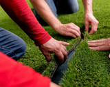 Two installers pressing an artificial turf seam together on a finished lawn