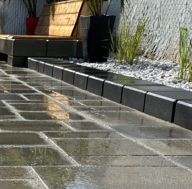 Rain-wet charcoal paver patio with tight stable joints and river rock border – all weather jointing sand result