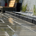 Rain-wet charcoal paver patio with tight stable joints and river rock border – all weather jointing sand result