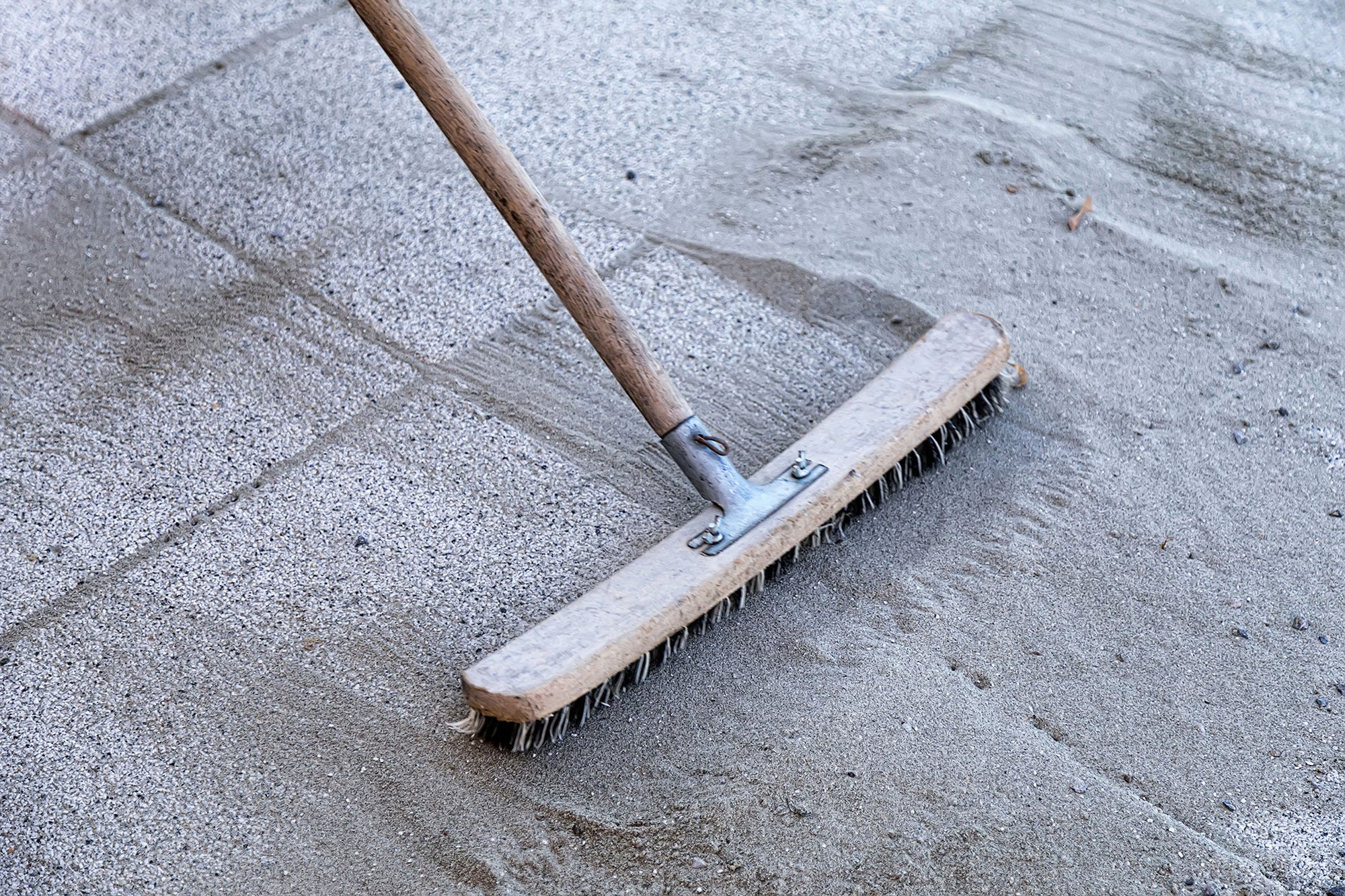 broom pushing polymeric sand into cracks between pavers